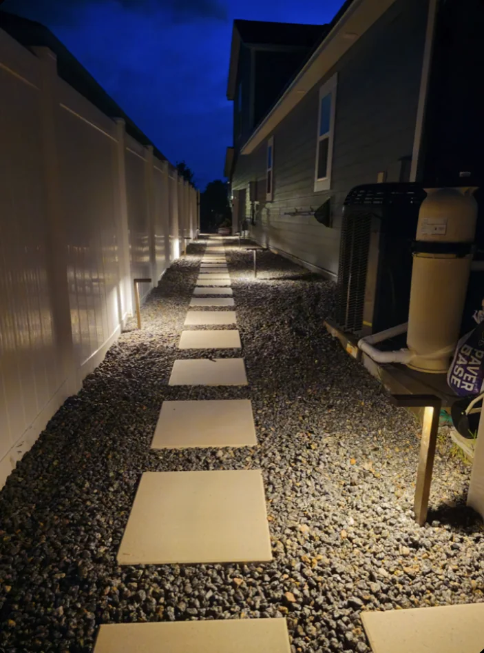 The side yard at dusk, lights along the fence base