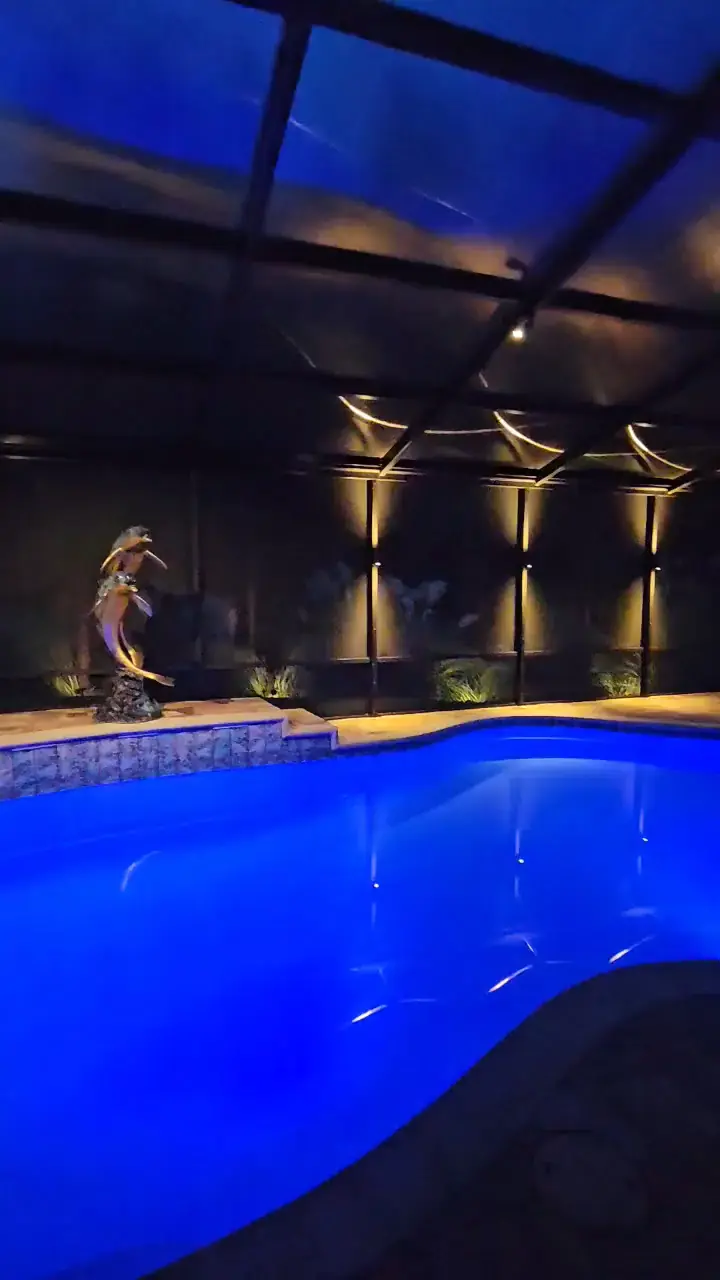 A slow pan across a screen pool enclosure at night, warm sconces on the frame and deep blue water